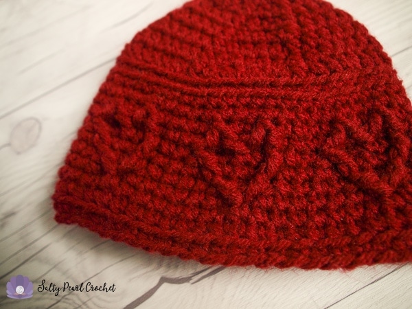 Red crochet newborn beanie with cabled hearts on a white wood background