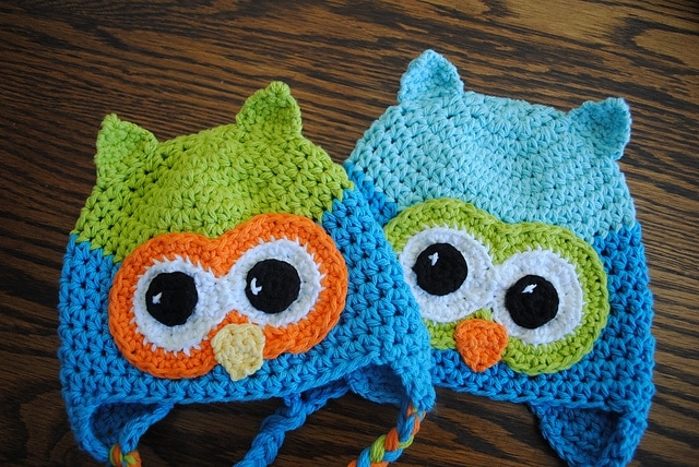 Two crochet owl beanies displayed on wooden background. 