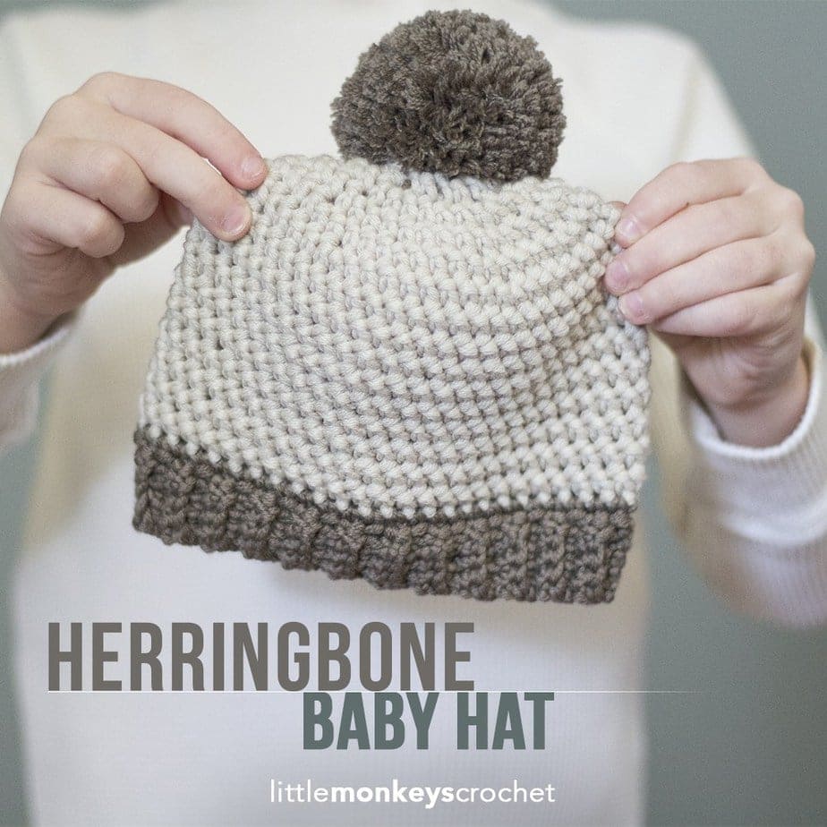hands holding a crochet herringbone stitch baby beanie that is cream with brown handmade pom and brown brim