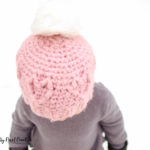 girl in the snow wearing a pink crochet heart hat with a pompom