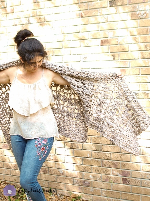 Woman wearing a tan poncho standing in front a brick wall outside. 