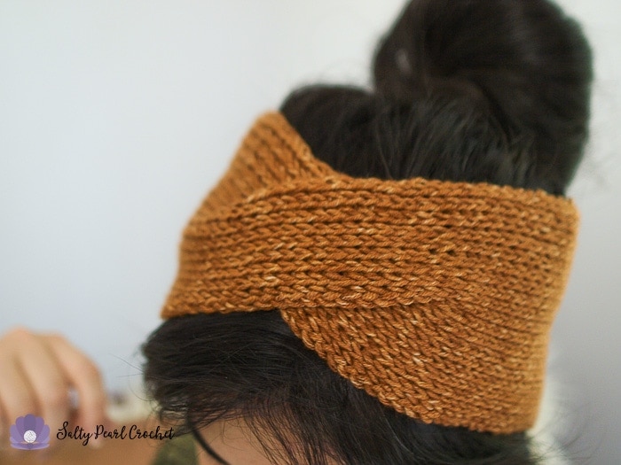 A close up of a woman wearing a crochet headwrap with a messy bun hairdo.