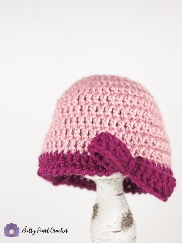 Light pink crochet beanie hat with dark pink brim and bow. 