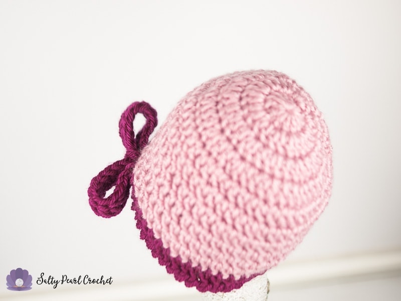 Close up of the back of a light pink crochet hat with a dark pink bow.