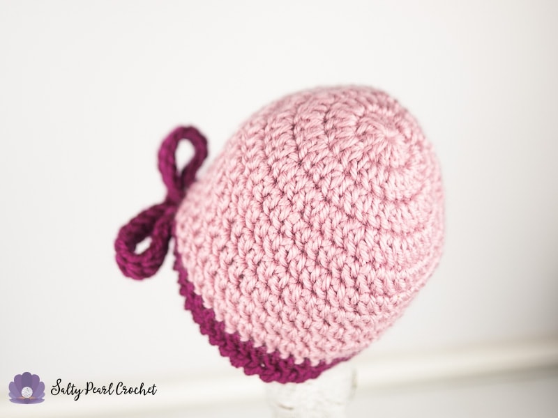 Close up of the back of a light pink crochet hat with a dark pink bow.
