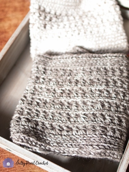 White crochet beanie and gray crochet cowl displayed in wooden serving tray on a table. 