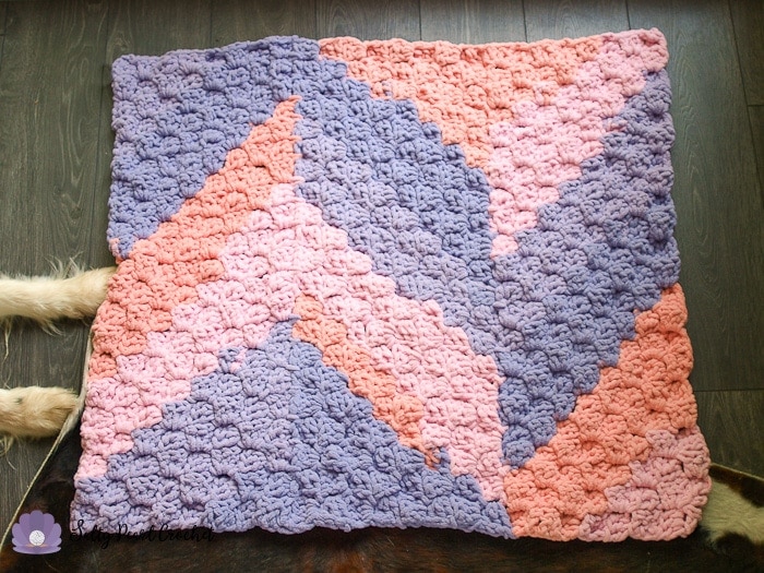 Pink and purple crochet blanket on wood floor. 