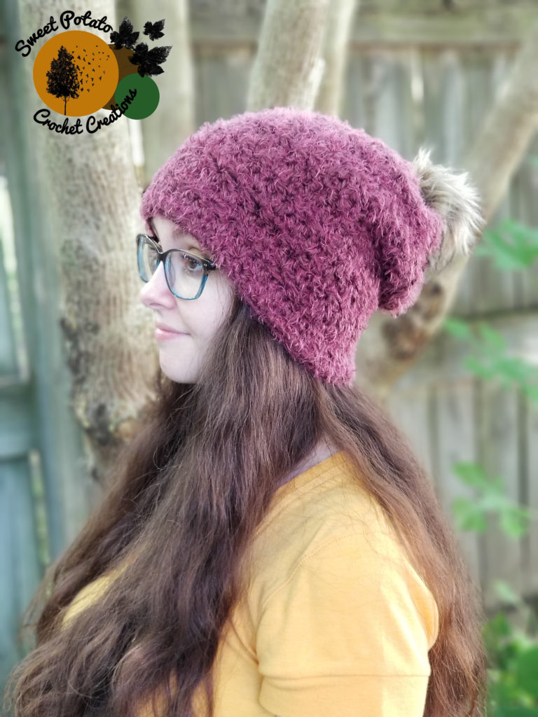 Girl wearing a fuzzy magenta crochet beanie with faux fur pom. 