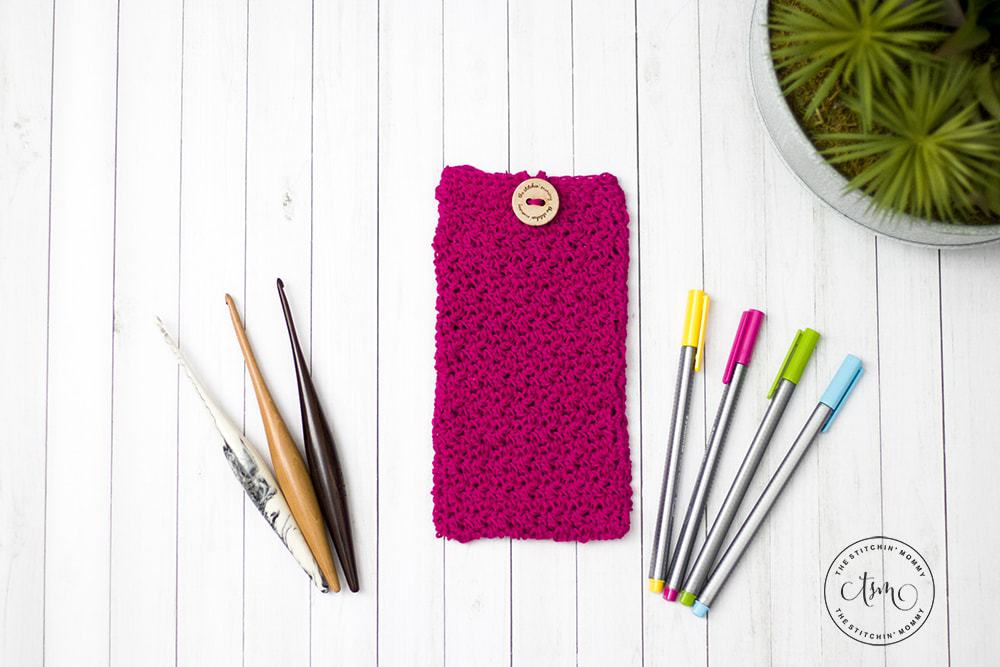 Magenta crochet pencil pouch, pens and wooden crochet hooks on white wood background. 