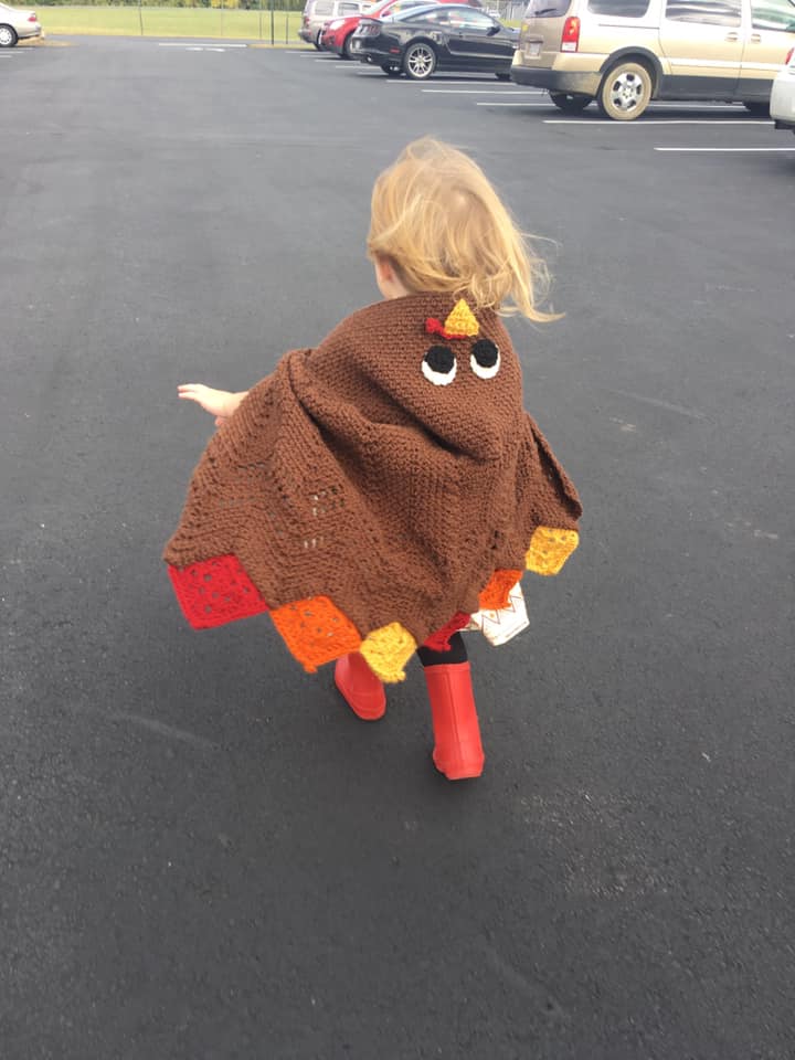 Little girl wearing a crocheted turkey hooded cape. 