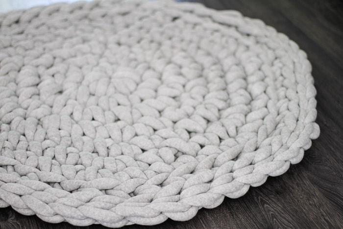 Close up of gray crochet round rug showing detail of stitches on a dark hardwood floor. 