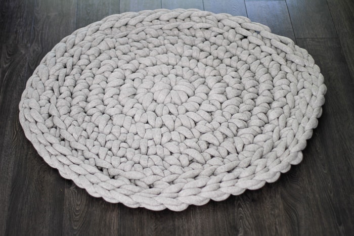 Large light gray round crochet rug on dark hardwood floor. 
