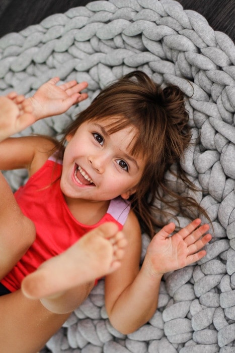 Little girl laying on gray crochet round rug smiling. 