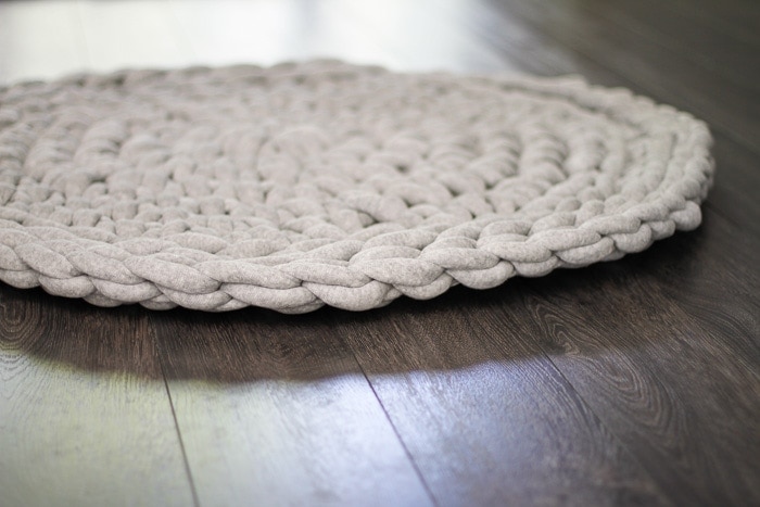 Close up showing the detail of side stitching of gray round crochet rug on hardwood floor. 