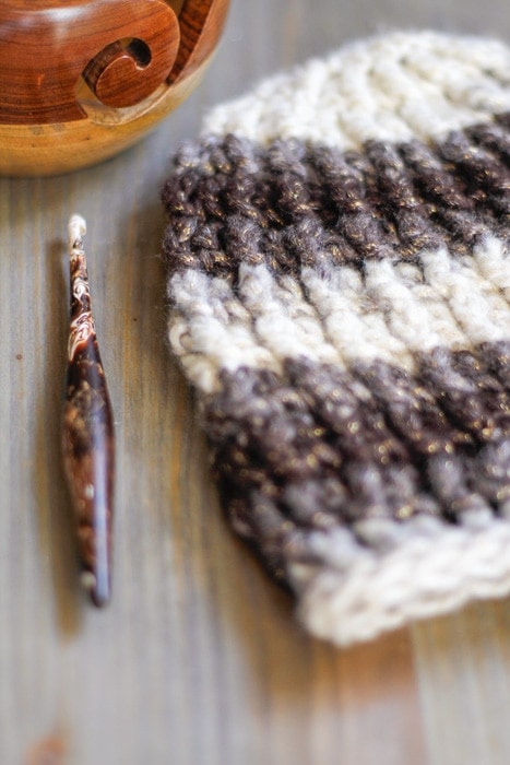 Crochet hook, yarn bowl, and a textured crochet beanie on a desktop.