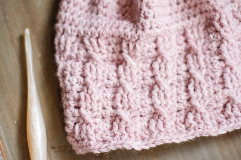 Closeup photo showing the crochet cable braid stitch on a pink beanie.