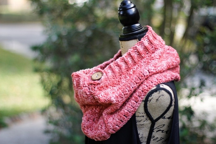 A crochet cowl pattern with a large button and crochet ribbing around the top edge on a dressform.