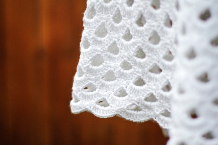 Closeup of the crochet collonade stitch lace pattern on a white poncho.