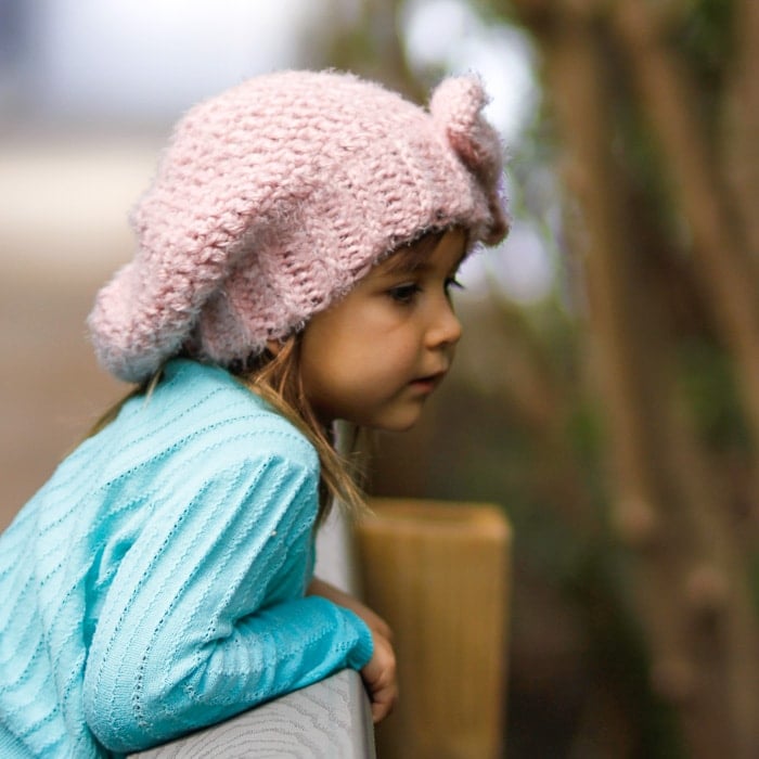 Girl wearing a pink crocheted slouchy hat with a bow looking over the side of a bridge.