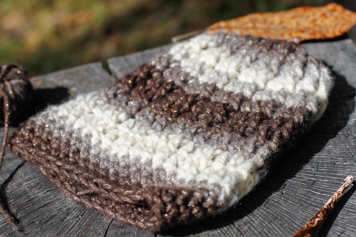The Uptown Coffee Beanie pattern displayed on a stump with a crochet hook, yarn and some leaves.
