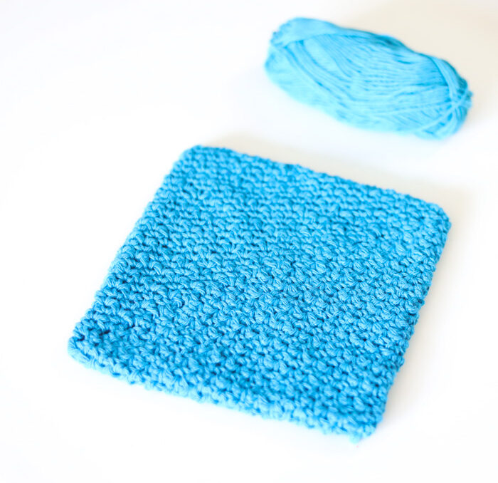 A crochet lemon peel stitch potholder with a ball of yarn