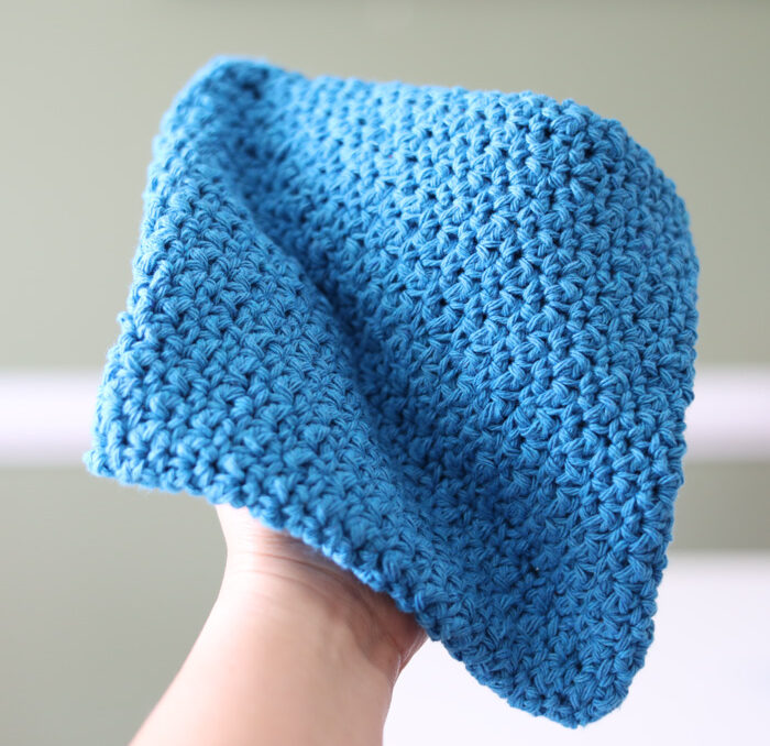 A hand holding a turquoise crochet potholder