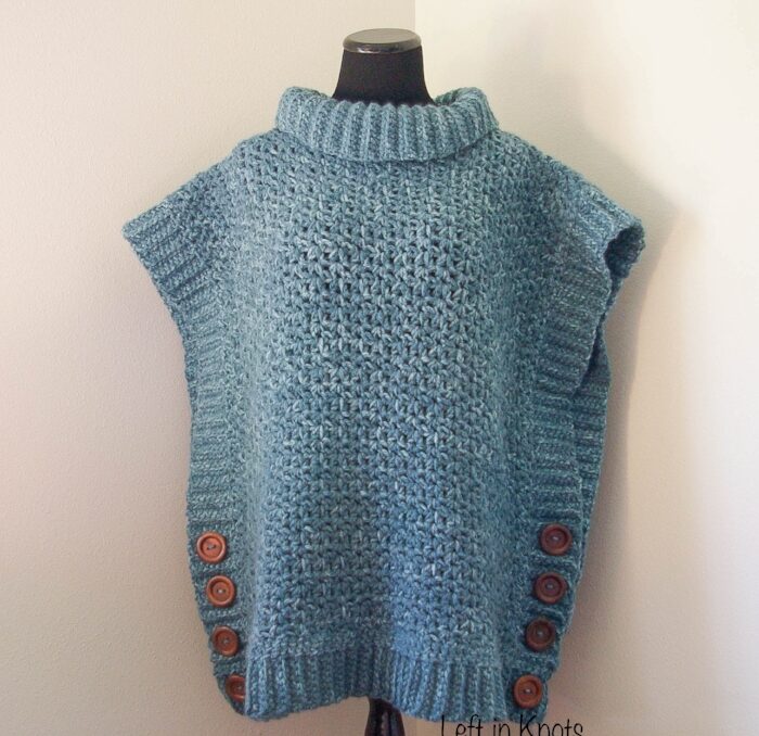 A blue crochet poncho with wooden buttons displayed on a mannequin. 