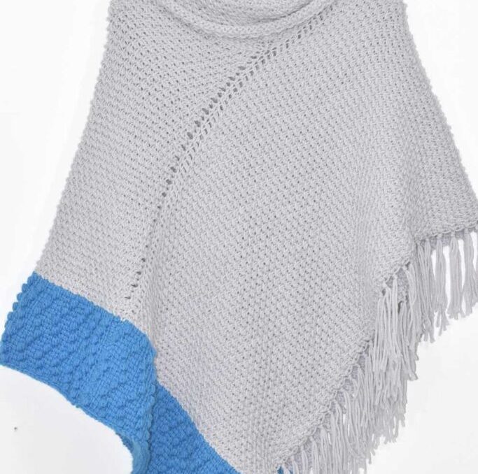 A crochet gray poncho with blue accent color edging with fringe.