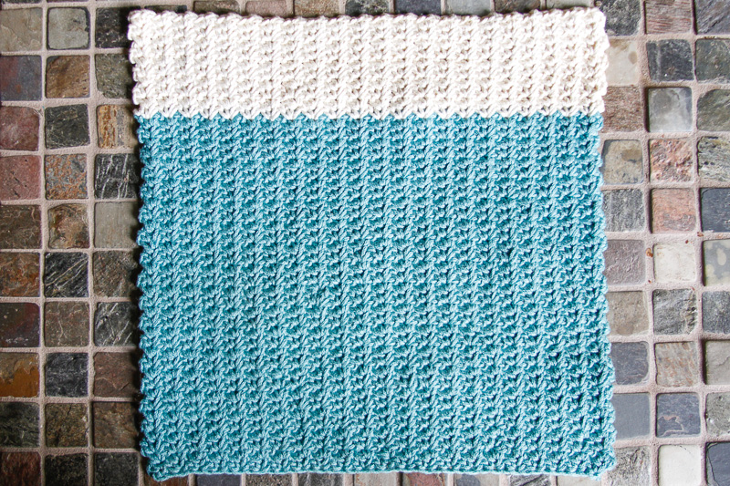 Blue and white crochet spider stitch dishcloth on a stone tile surface.