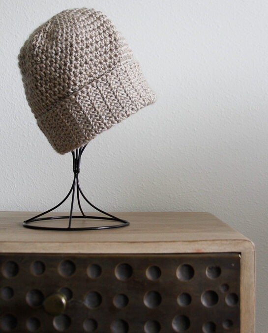 A tan hat with a folded up brim displayed on a hat holder