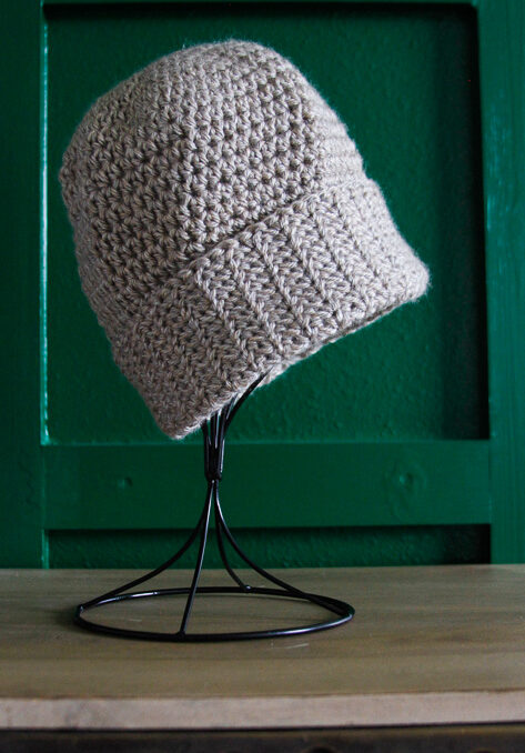 Tan crochet hat displayed on a table top hat stand. 