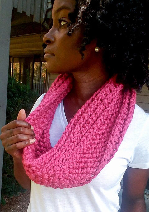 Woman wearing a pink crochet cowl standing outside. 