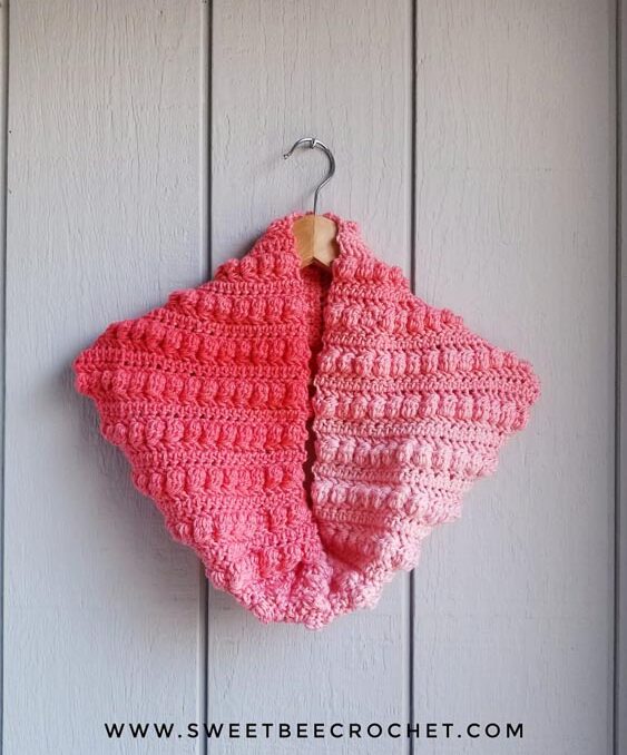 A pink cowl crocheted from color changing yarn using crochet bobble stitches.