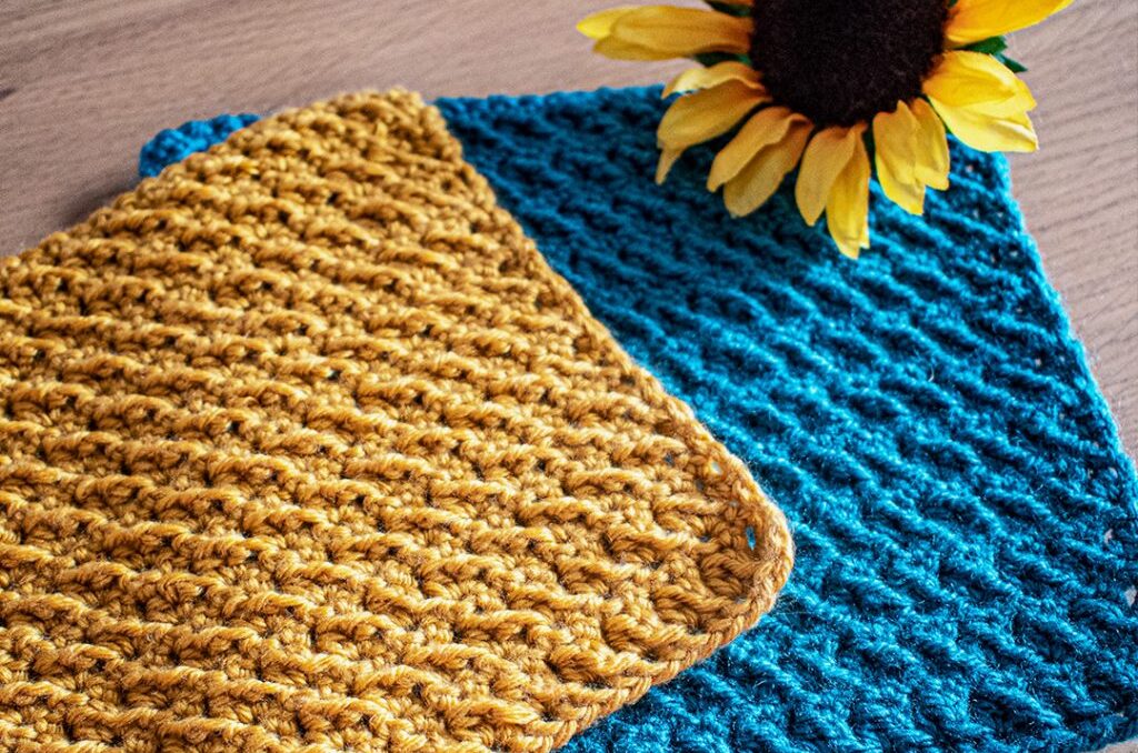 a yellow crochet washcloth lying on top of a matching blue washcloth with a sunflower