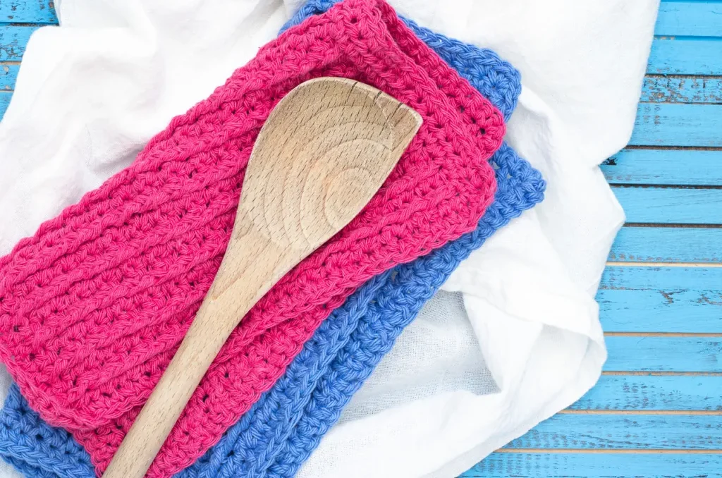 Crochet dishcloths with cable stitches stacked beneath a wooden spoon