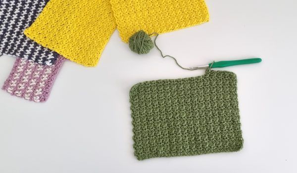 a progress shot of a green crochet washcloth project laid out beside ot her finished washcloths