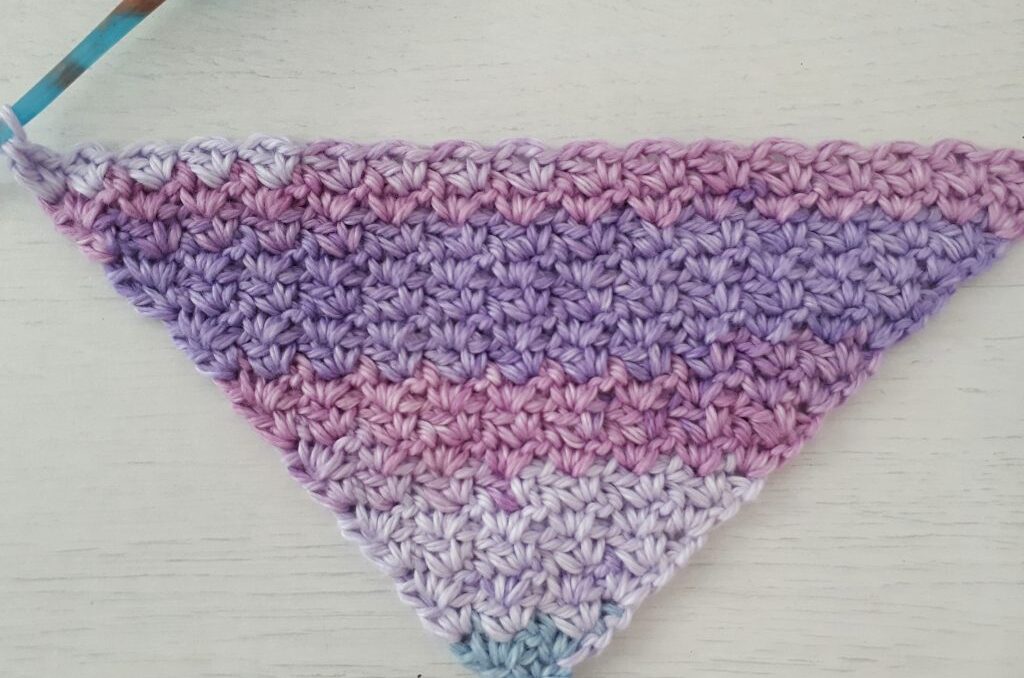 a progress shot of a corner to corner crochet washcloth pattern, with a crochet hook at the top left corner