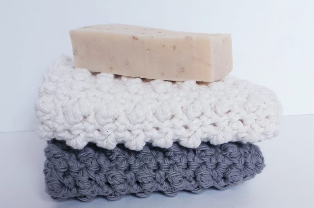 A stack of textured crochet washcloths beneath handmade soap.