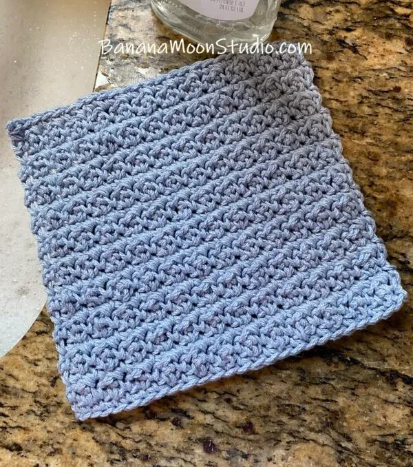 a blue crochet washcloth on the side of a granite sink