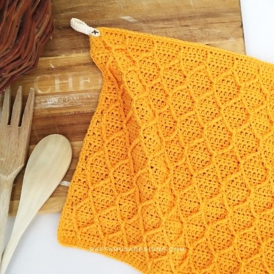 A yellow honeycomb stitch dishcloth on a wooden cutting board