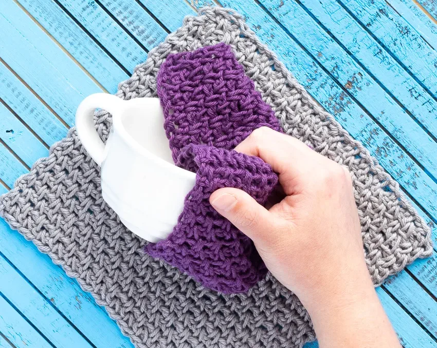a hand uses a purple crrochet dishcloth to clean a teacup