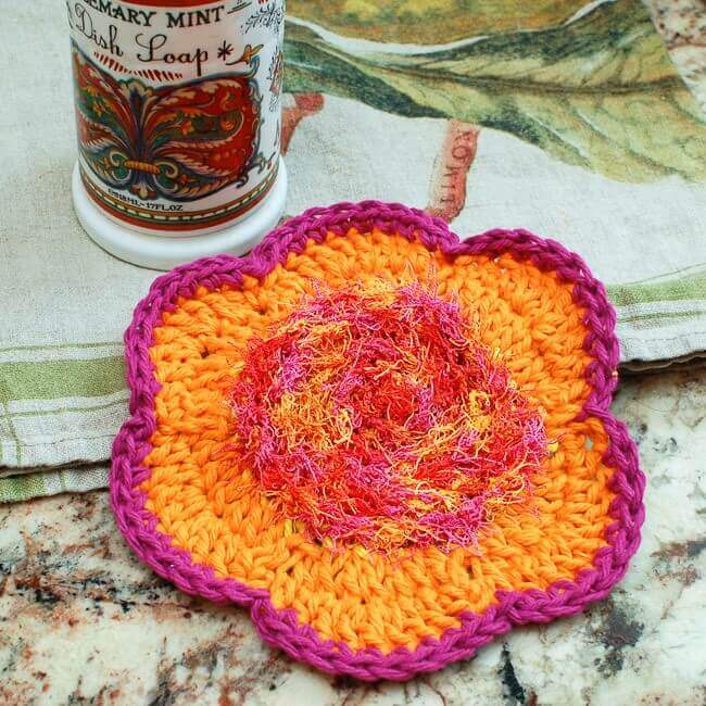a pink and orange flower shaped crochet dish scrubby
