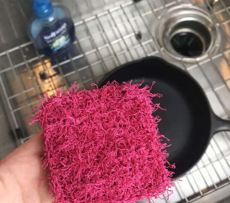 a pink crochet dish scrubber over a sink with a cast iron skillet inside