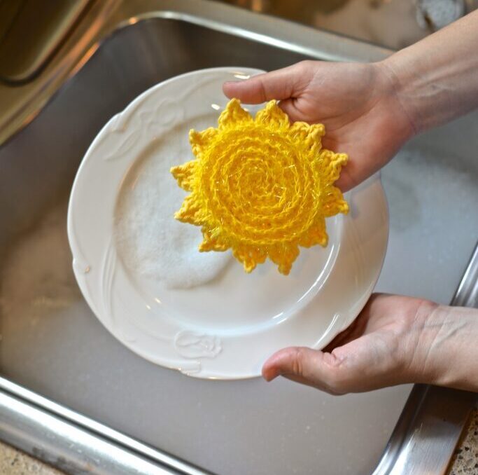 a sun shaped yellow dish scrubber washing a plate