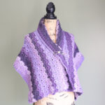 A purple crochet lace shawl wrapped on a mannequin using a shawl pin.