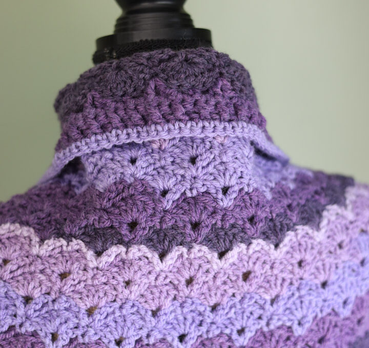 Close up photo of the shawl collar of a purple crochet lace shawl.