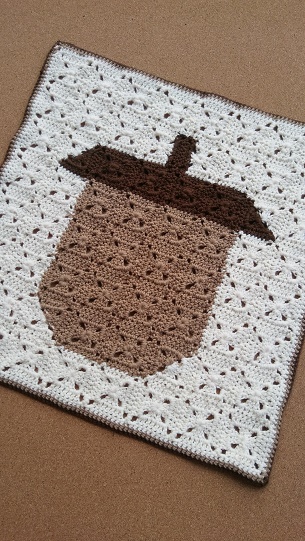 A crochet blanket with different color squares making an acorn pixel art.