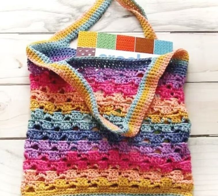 a colorful striped crochet market bag holding a book