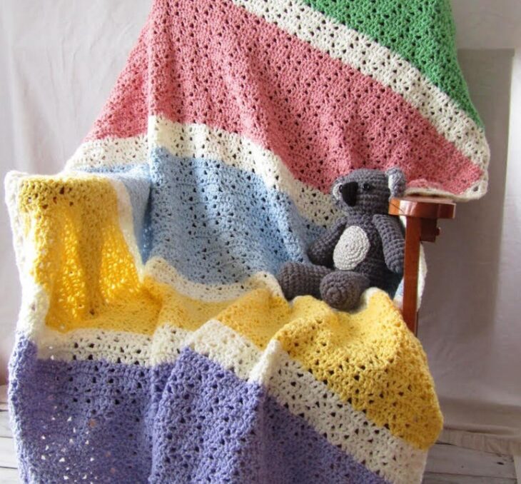 a striped crochet toddler blanket on a rocking chair with a stuffed toy