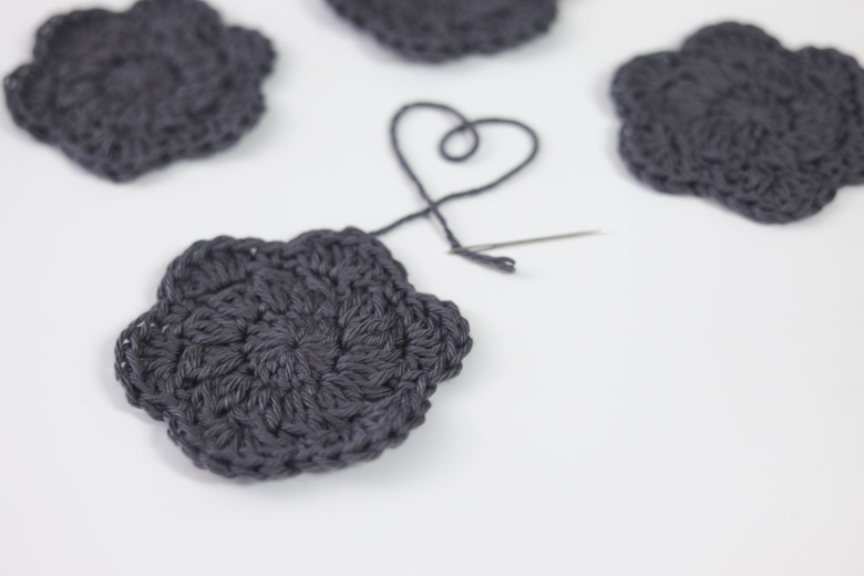 a loose yarn end forms a heart on a crochet face scrubby laid on a table with 3 finished scrubbies